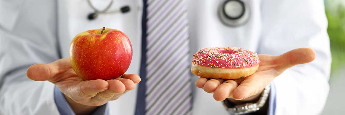 A doctor holds a red apple in one hand and a pink frosted donut in the other.