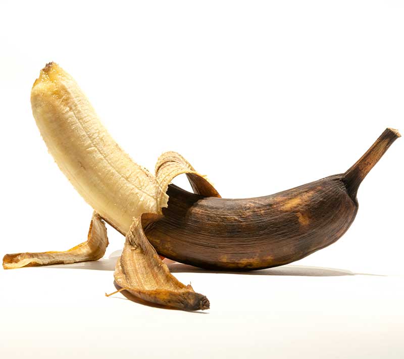 A partially peeled banana with a dark brown peel and light yellow fruit.