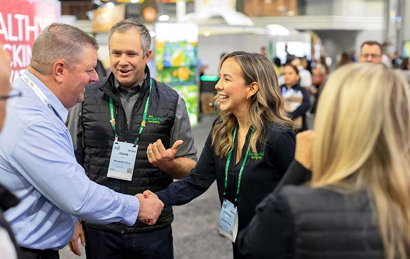 People shaking hands at The Global Produce and Floral Show, surrounded by attendees and booths.