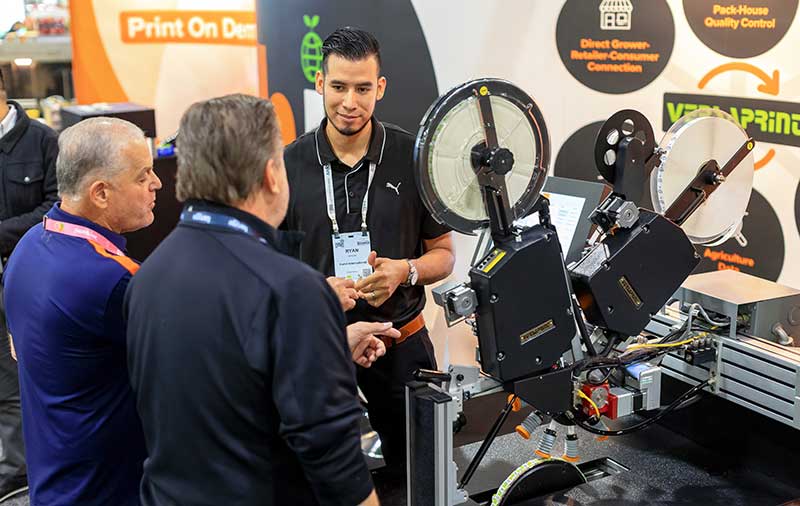 Three men at a trade show discussing a labeling machine.